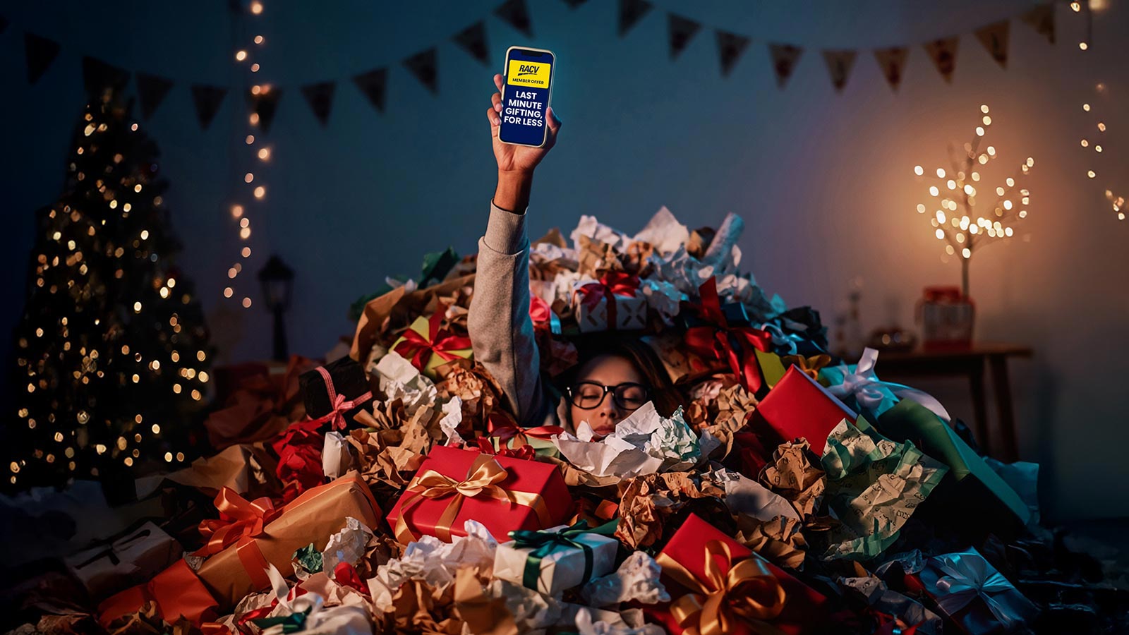 A woman sinking in wrapping paper holding her phone up in the air. 
