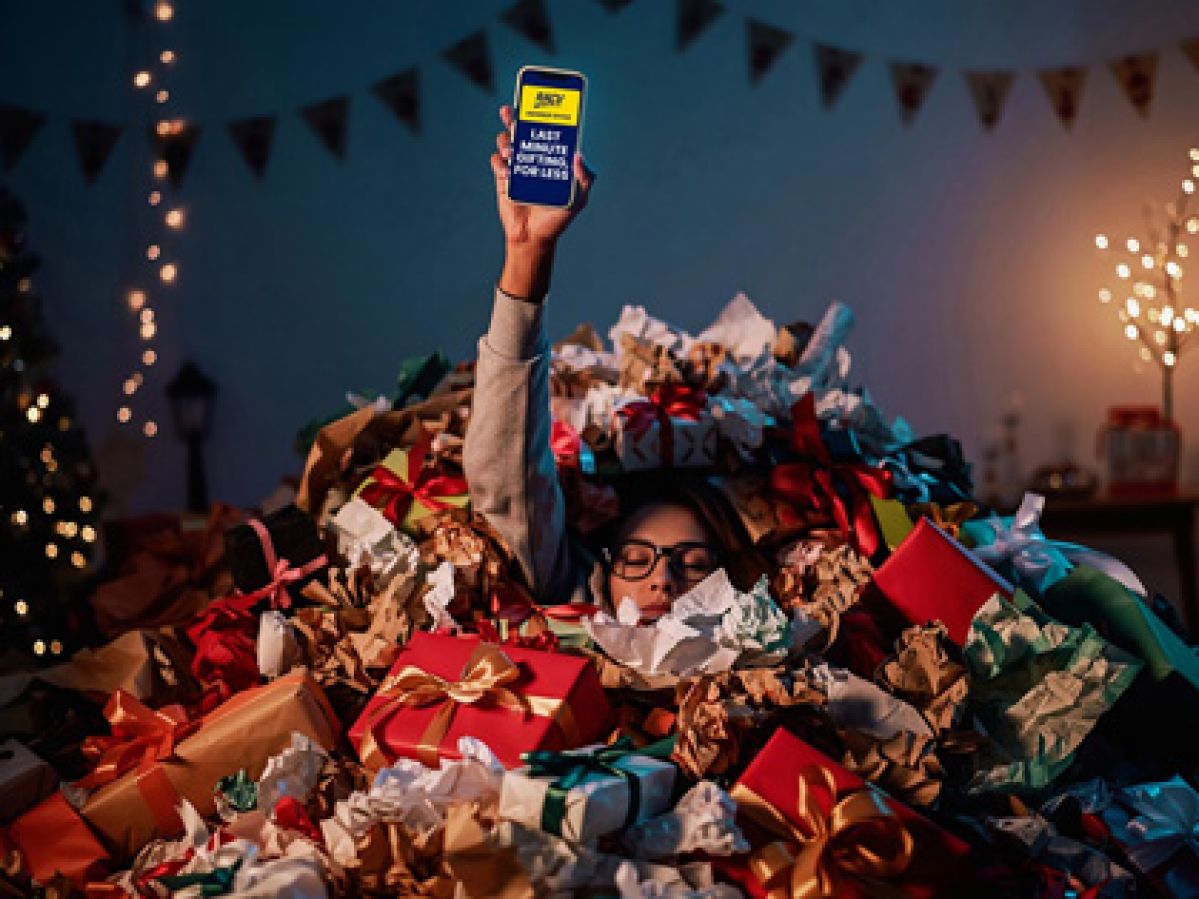 A woman sinking in wrapping paper holding her phone up in the air. 