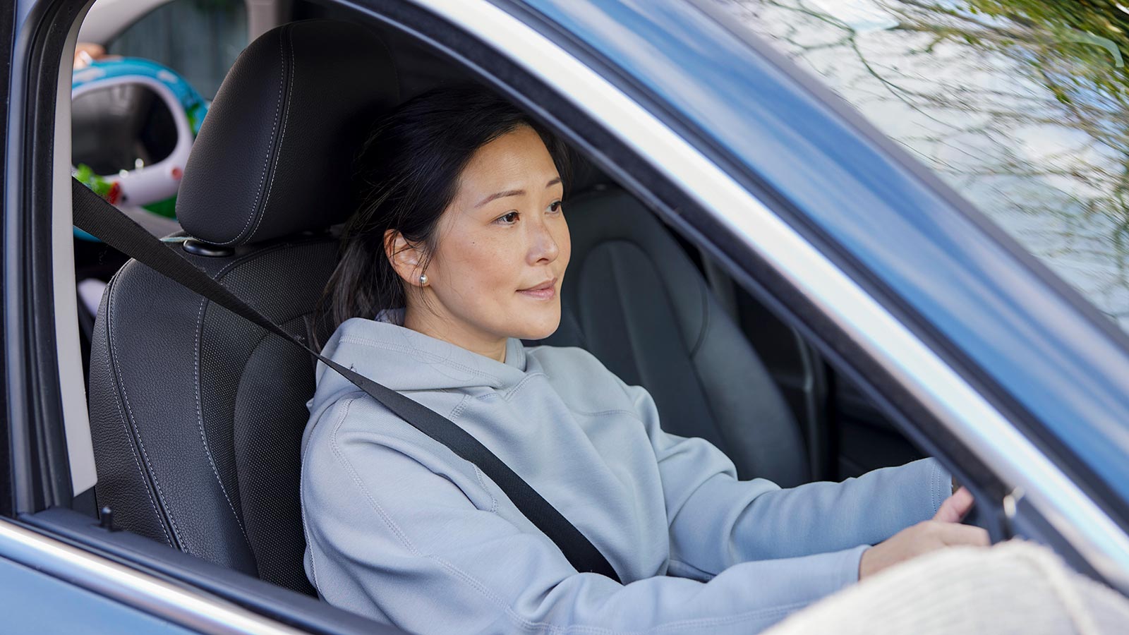 Person in a grey hoodie, sitting in the driver's seat of a blue car.