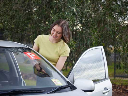 Young woman putting P plates in the front windscreen of a car.