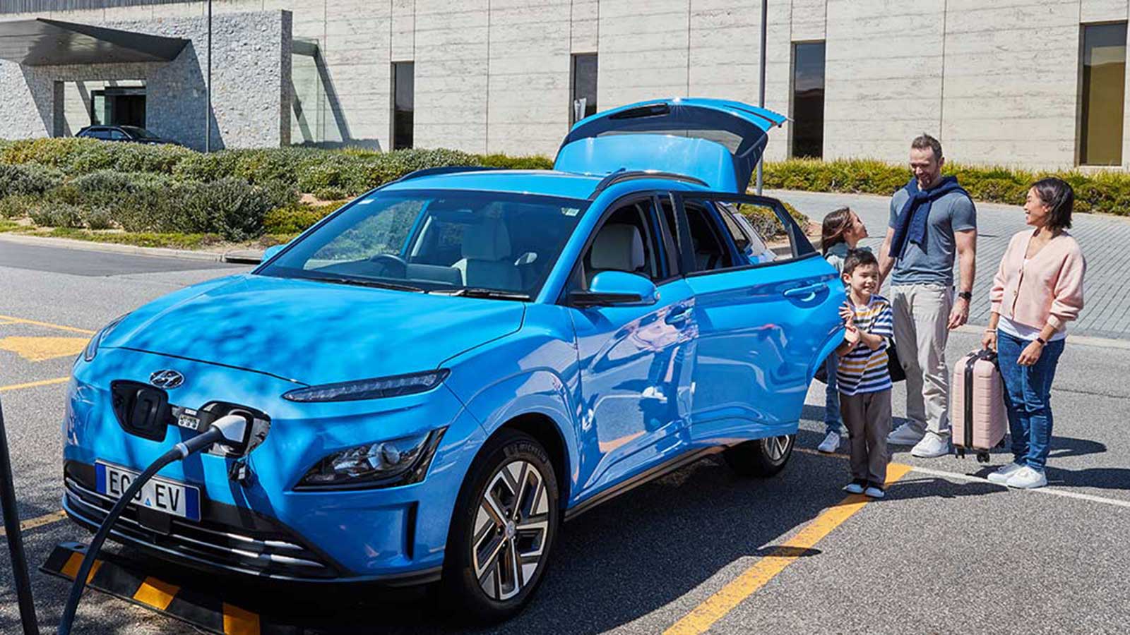 Family standing next to a blue electric vehicle as it charges.