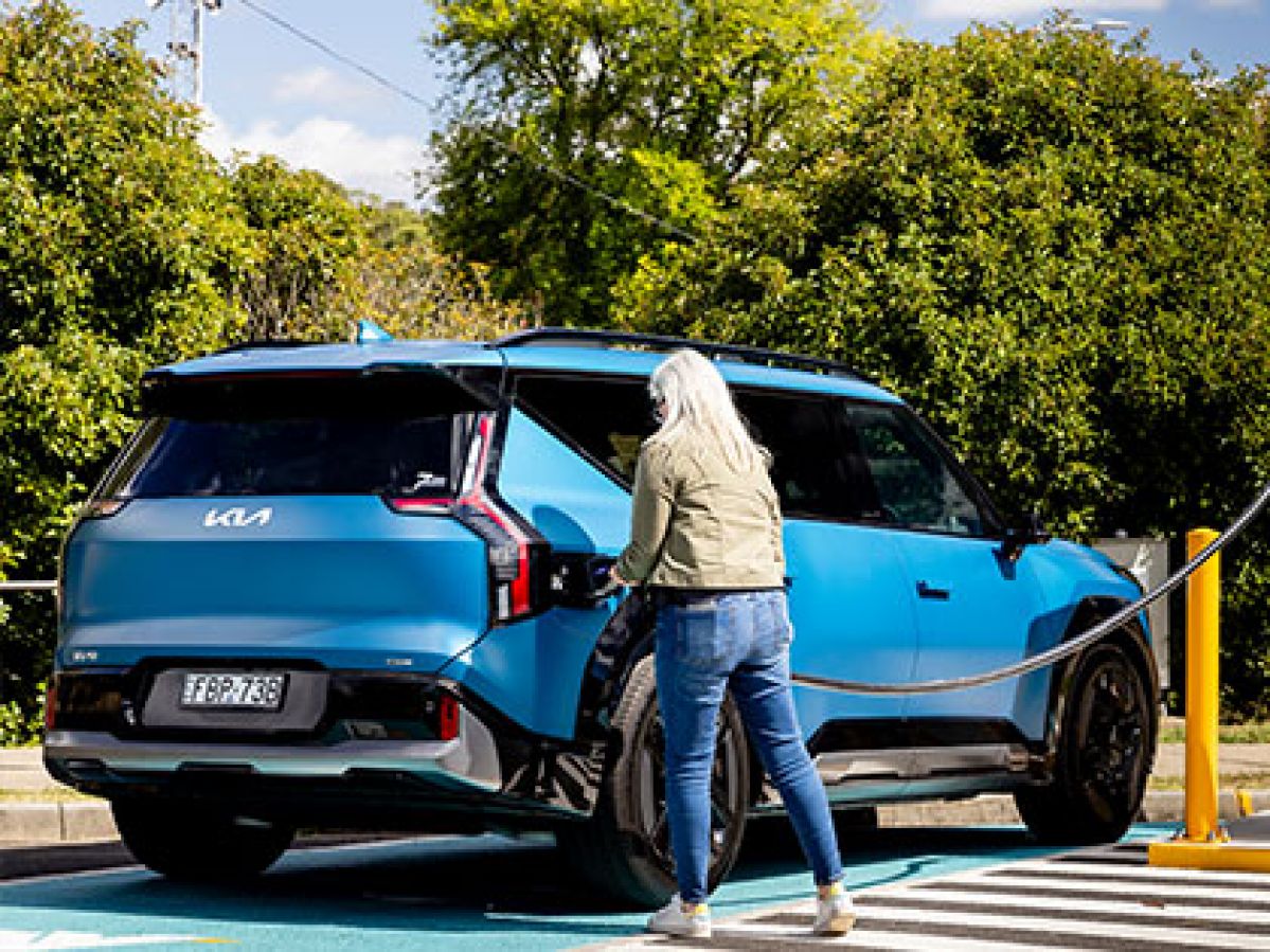 Woman holding an EV charger next to a blue Kia EV9. 