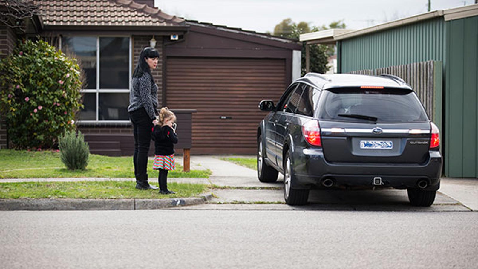 A mother holding her child's hand whilst a car is reversing.