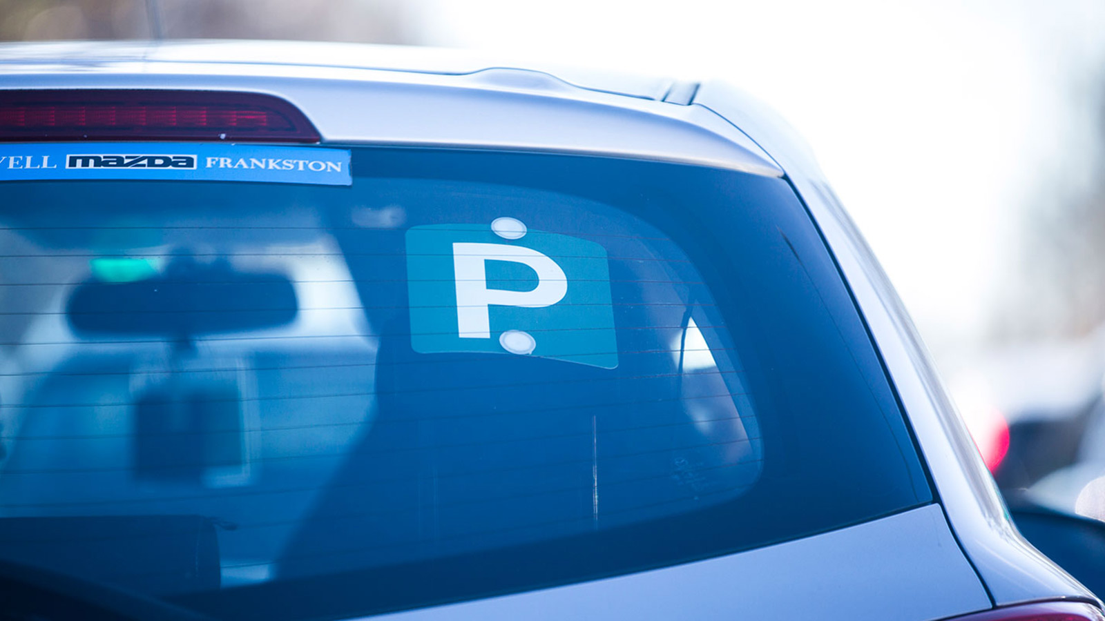 Green P plate on the rear window of a silver car.
