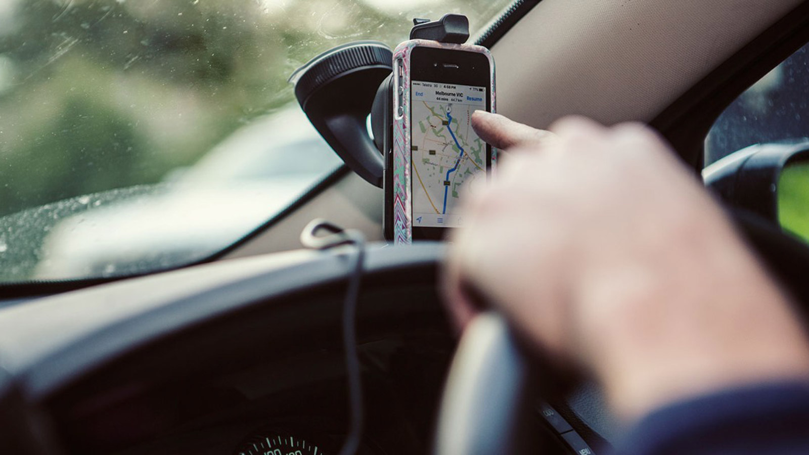 Dashboard with a person about to touch the mounted phone displaying maps.