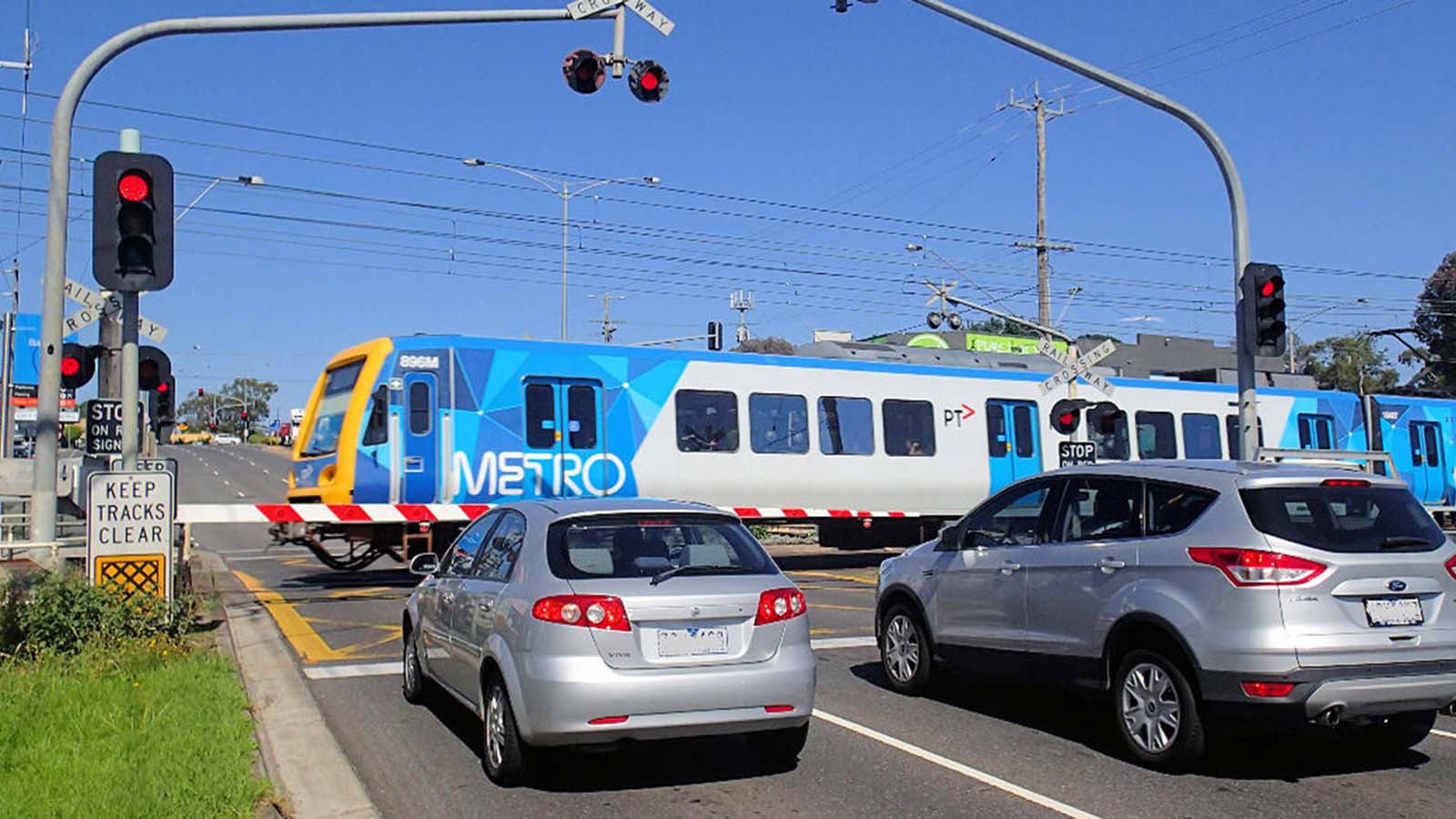 Cars waiting for Metro train to pass at level crossing.