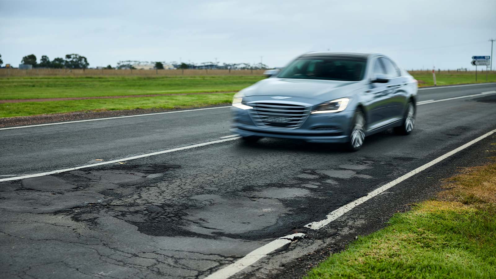 Car driving along a regional road near potholes.