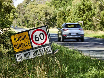 Car driving on a country road past a rough surface warning sign.