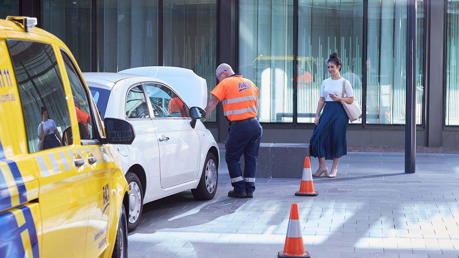 RACV technician fixing a car and speaking to a smiling customer outside of an office building.