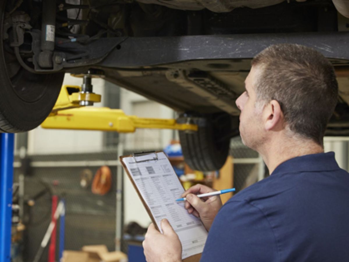 A mechanic with a clipboard assessing a vehicle.