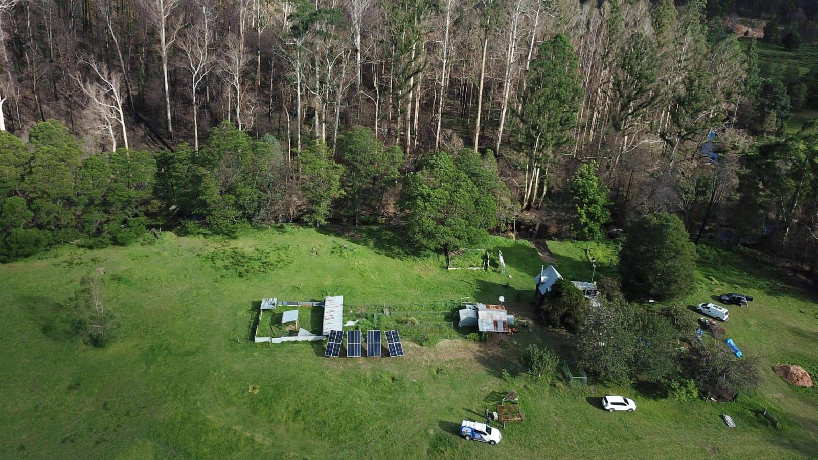 An aerial shot of Victorian countryside, featuring an open green space surrounded by trees, with small properties and solar panels on the green.