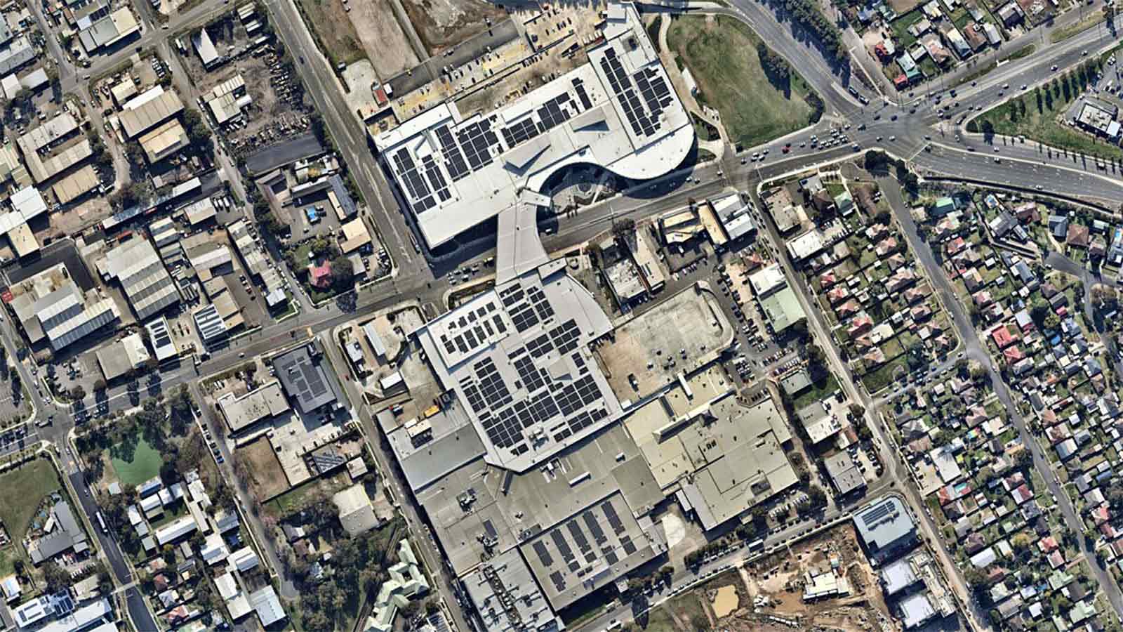 Aerial view of industrial buildings fitted with solar panels next to a roads and residential buildings. 