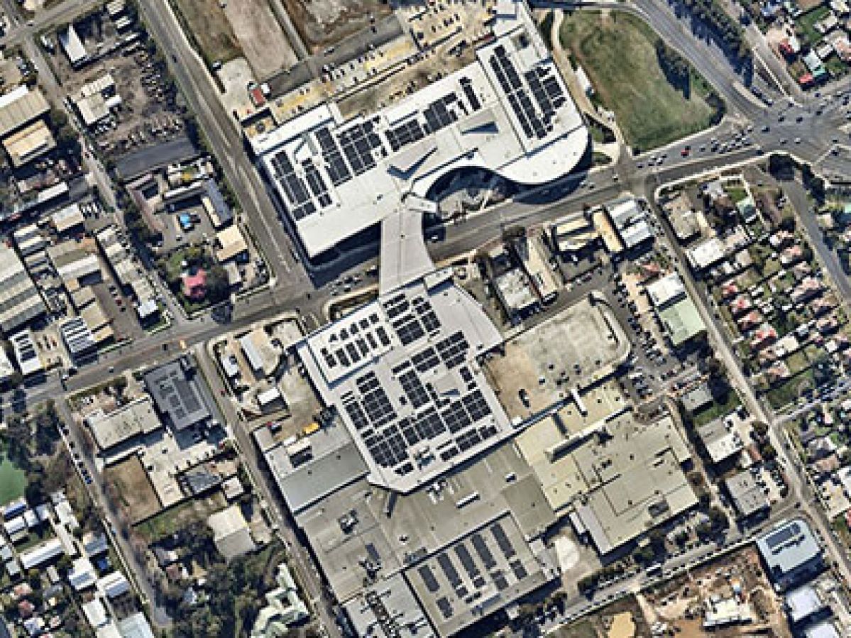 Aerial view of industrial buildings fitted with solar panels next to a roads and residential buildings. 