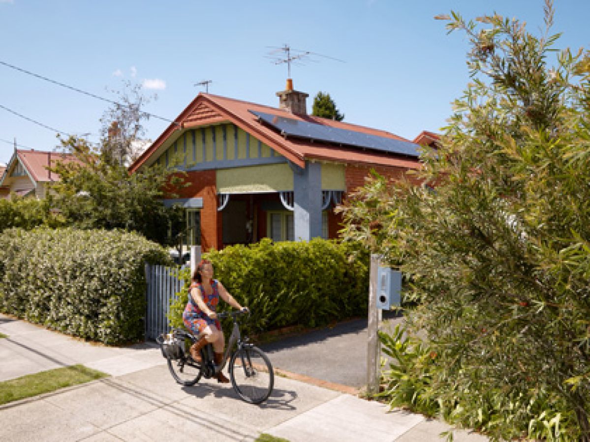 A person riding their bike while passing a residential house with solar panels.