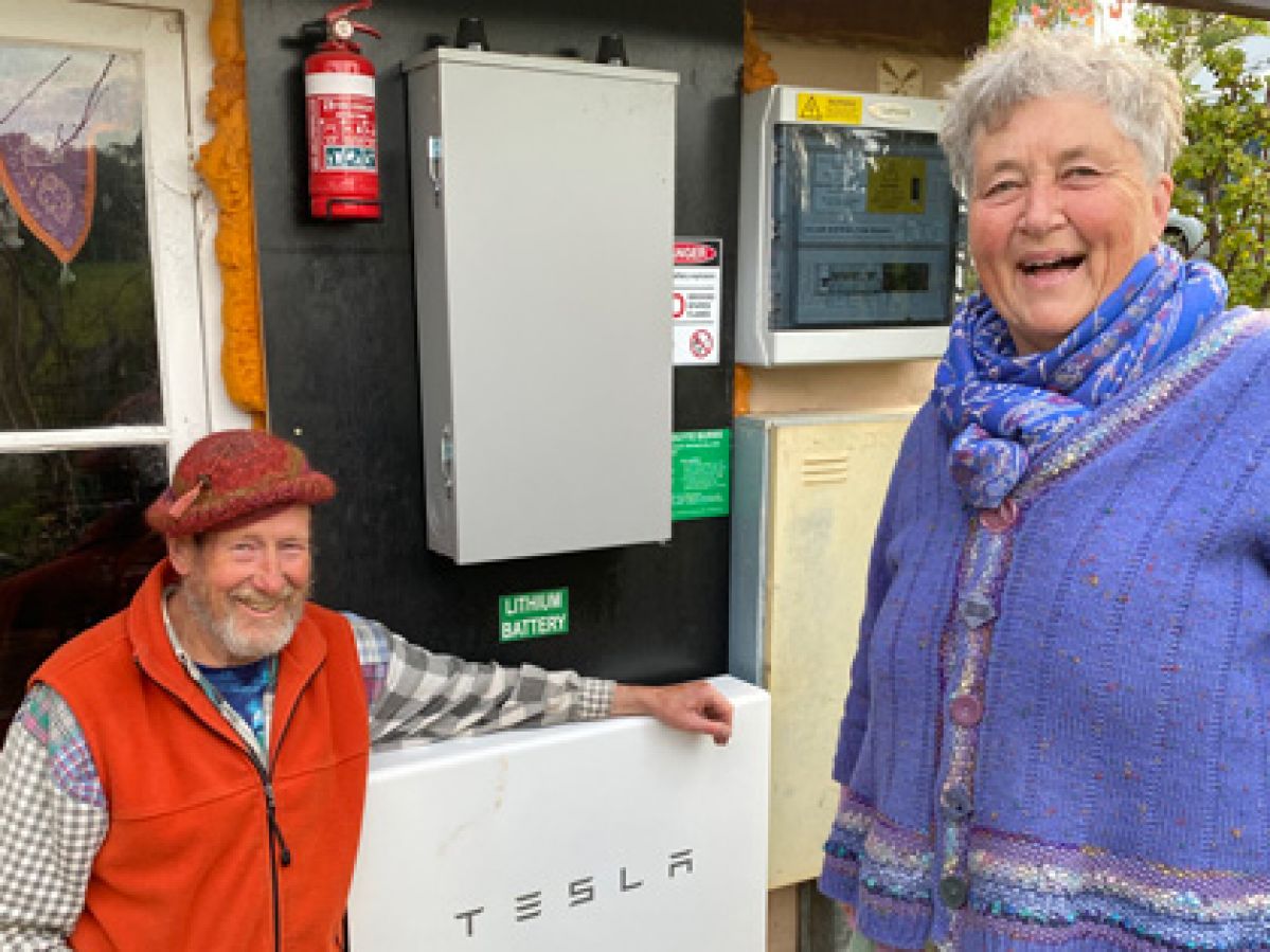 A smiling couple stand next to Tesla powerwall battery.