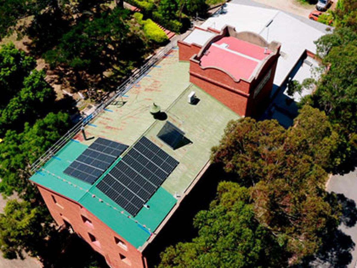 Solar panels on the roof of the Yea Butter Factory building, surrounded by lush greenery. 