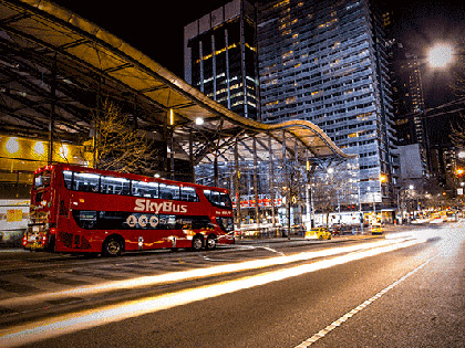 Melbourne Airport SkyBus parked near buildings at night.