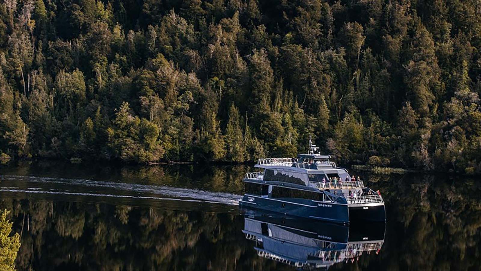 Ferry sailing down Gordon River, surrounded by tree-lined coasts.
