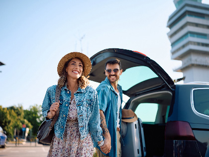 Happy couple taking their luggage from a car at airport parking lot.