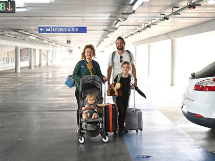A fmaily of three heading to the airport with their luggage from the carpark.