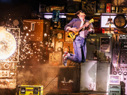 A man playing guitar on stage jumping in the air. 
