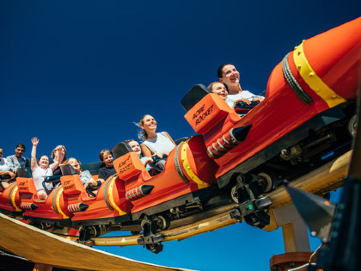 A group of people riding an orange and yellow roller coaster at Movie World.