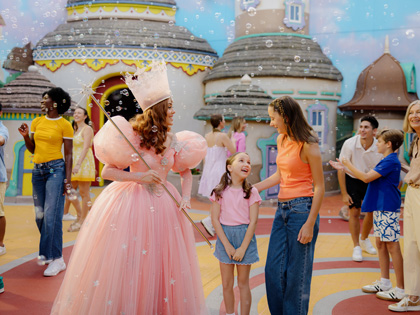 A character dressed as Glinda from the Wizaed of Oz at Village theme park talking to a young girl.