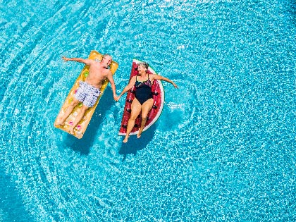 Aerial view of people a couple holding hands and floating in a blue clear swimming pool.