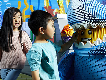 Two children looking at statue of a man in a whale suit made out of lego.