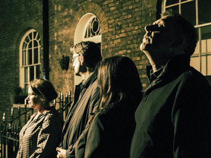 People stand outside in the dark infront of an old building.