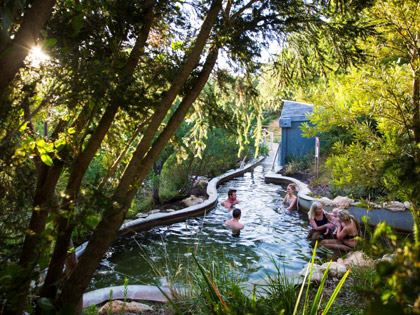 Several people relaxing in the springs designed to look like a river surrounded by lush greenery.