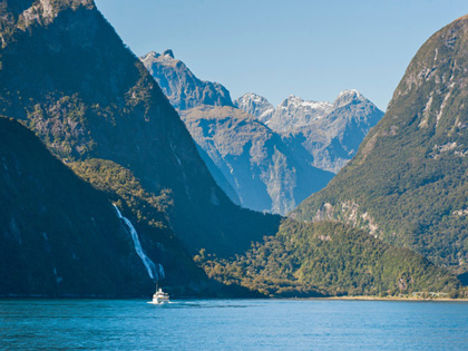 A boat in the distance of some picturesque waterfalls in queenstown 