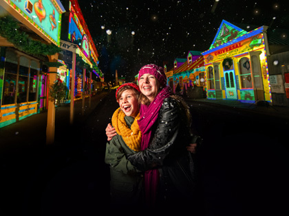 Two kids hugging at Sovereign Hill at night with colourful lights surrounding them.