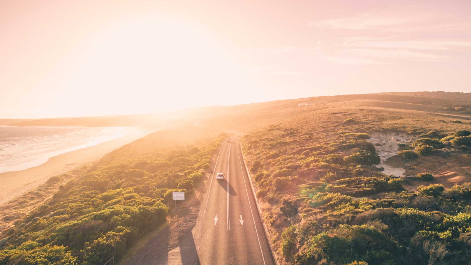 An aerial view of a car travelling on a road at dusk.