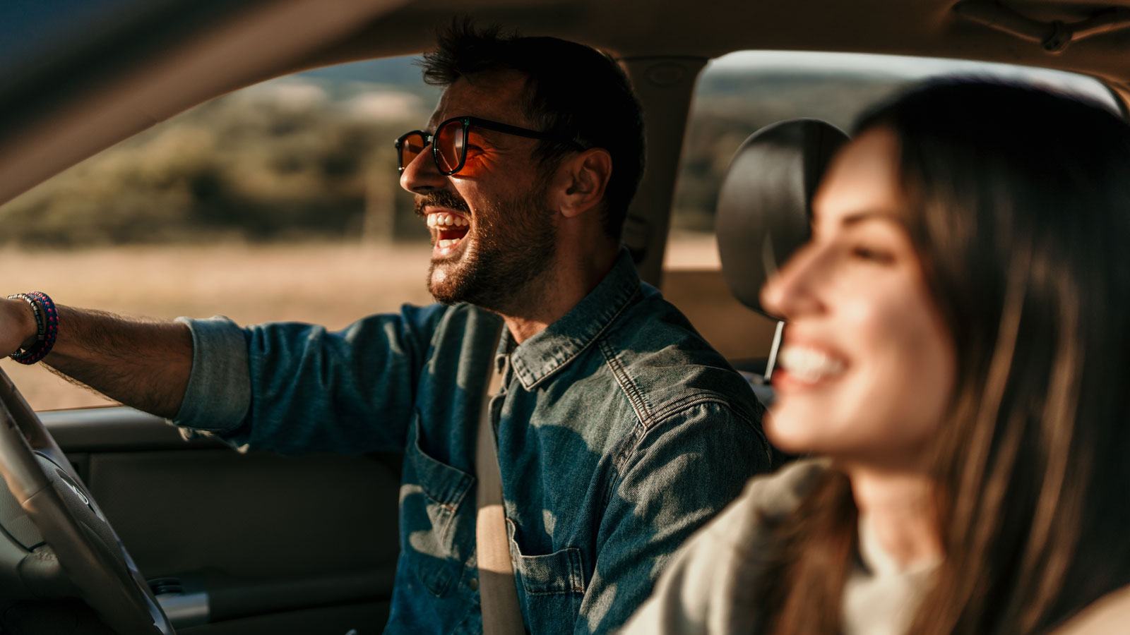 A couple in the front seat of a car laughing and smiling. 