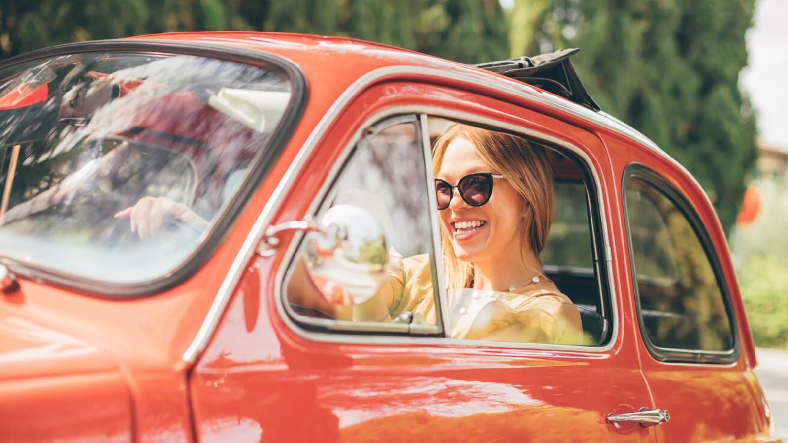 Woman wearing sunglasses sitting in a red, vintage car.