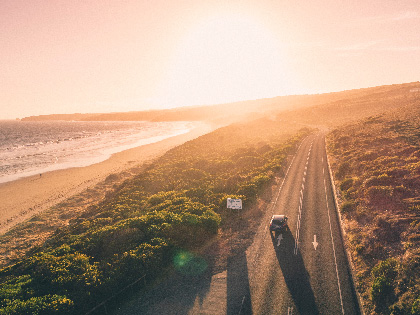 Aerial View of Great Ocean Road and a car driving into the sunset.