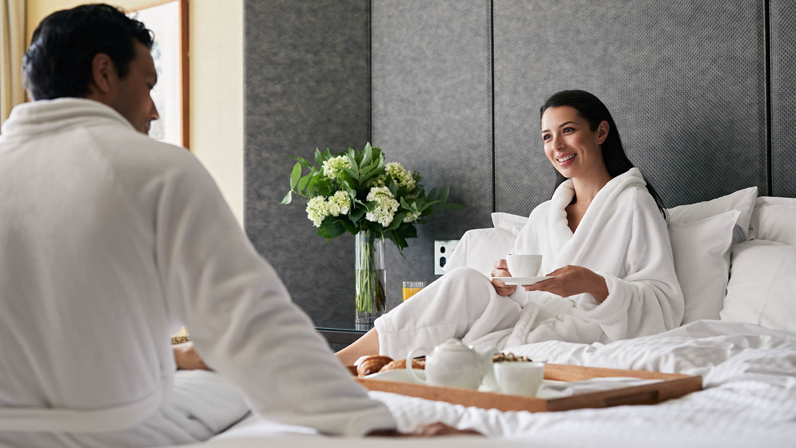 Couple wearing bathrobes enjoying a tray of tea in bed.