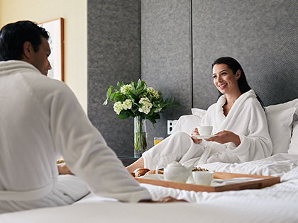Couple wearing bathrobes enjoying a tray of tea in bed.