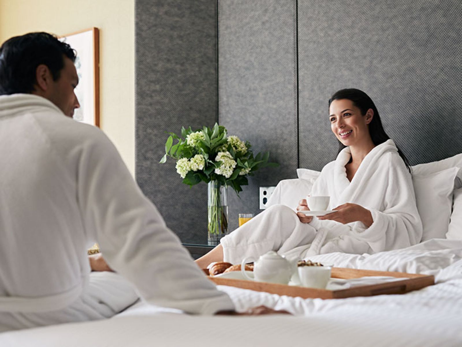Couple wearing bathrobes enjoying a tray of tea in bed.