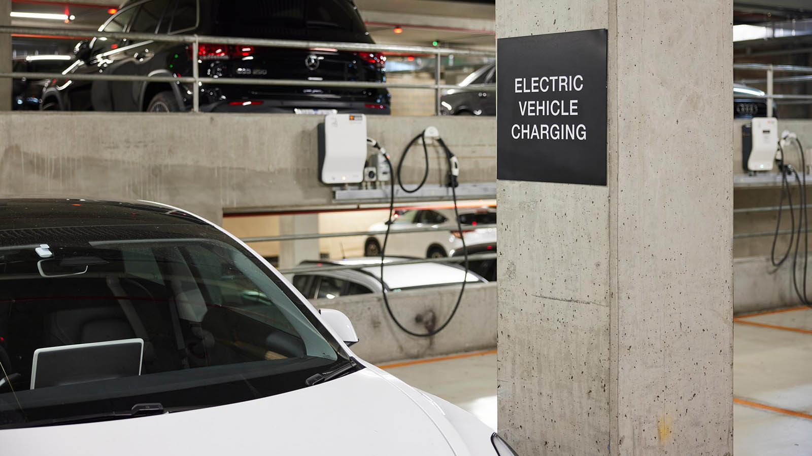 A white car in a carpark connected to an EV charger.