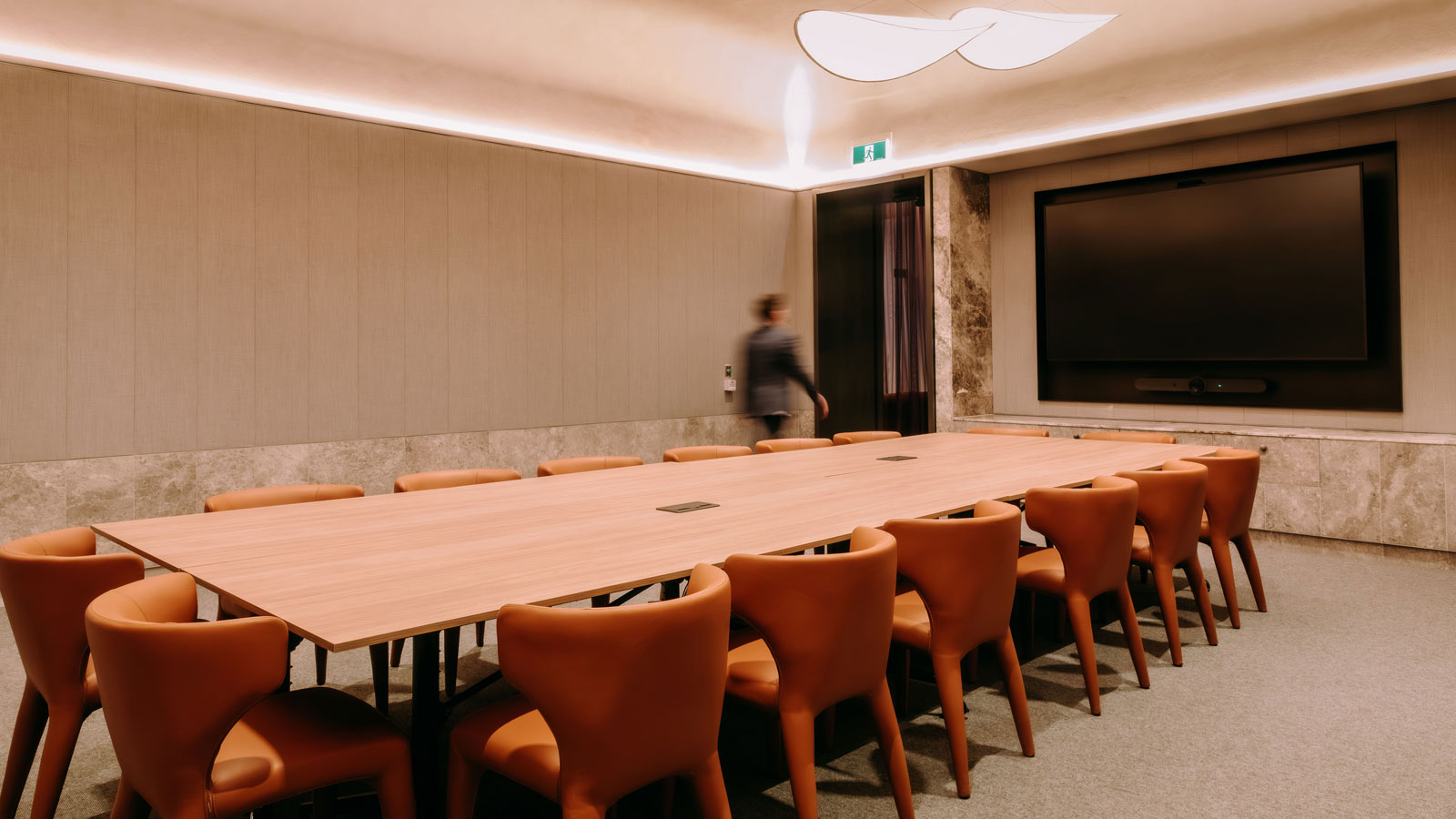 A table set in a meeting room with sixteen orange chairs and a screen.