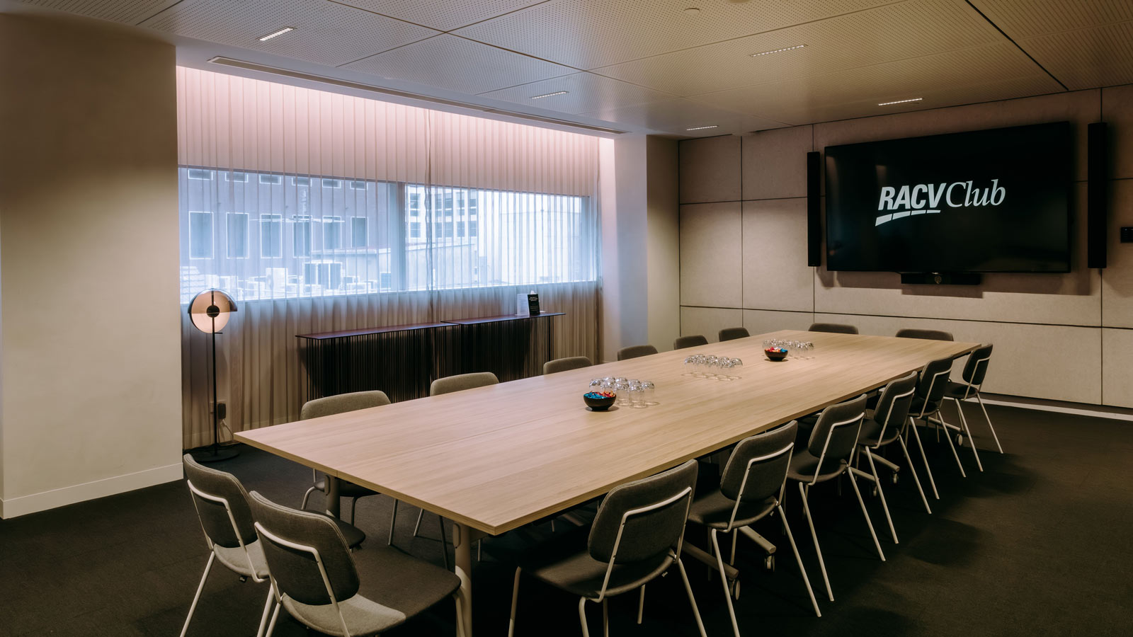 A table set in a meeting room with sixteen chairs and a screen.