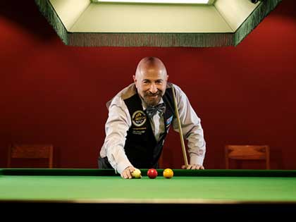 Resident champion billiard player smiling and standing by the billiard table.