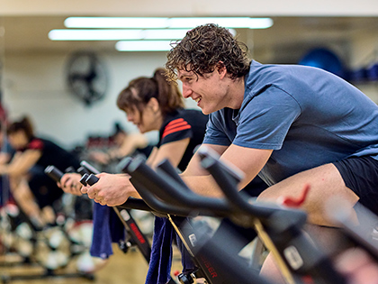People smiling while using exercise bikes in the fitness centre at RACV City Club.