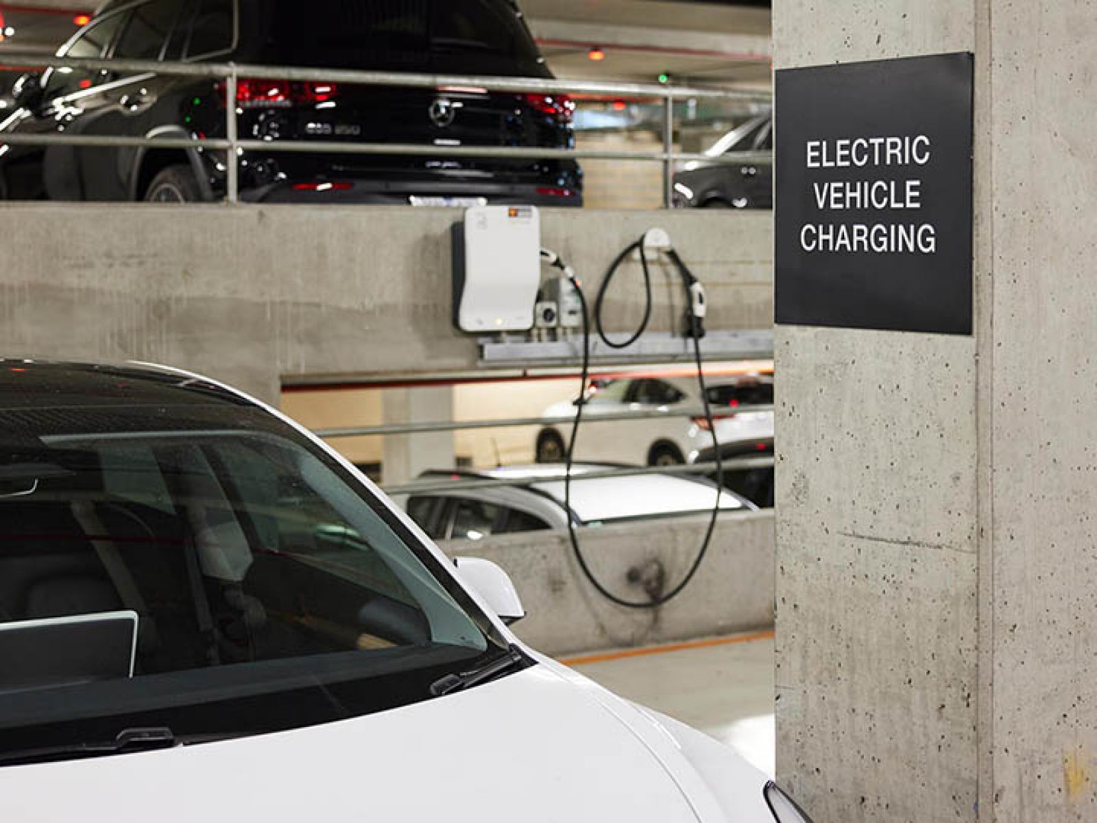 A white car in a carpark connected to an EV charger.