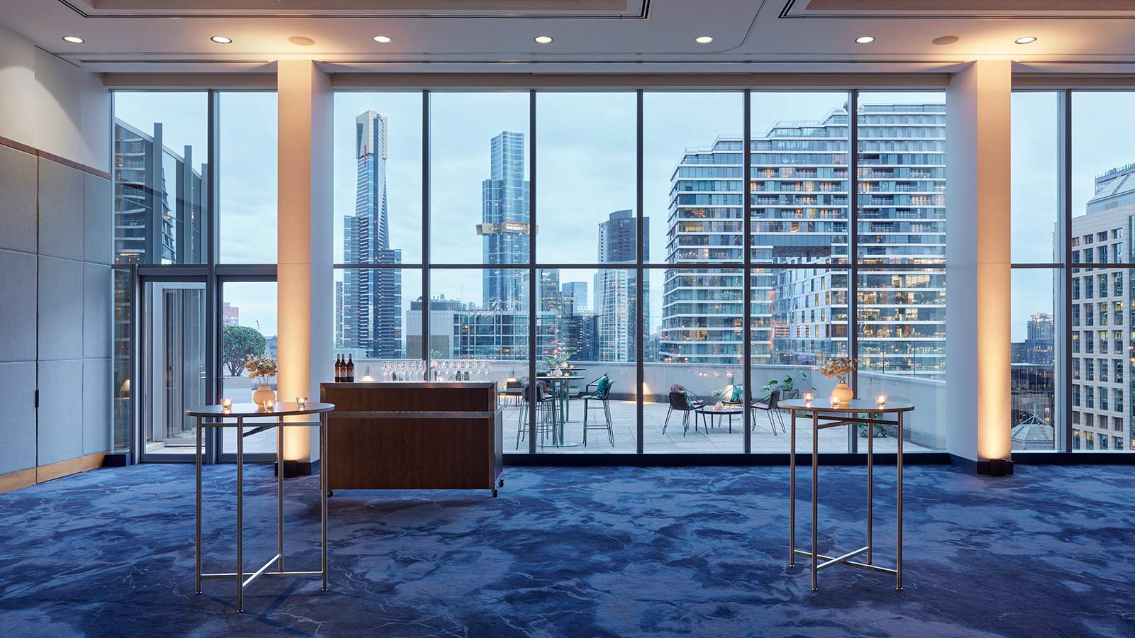Level 17 of RACV City Club set up for a cocktail event in the evening, with a cocktail station set up inside, and chairs and small tables on the balcony outside.