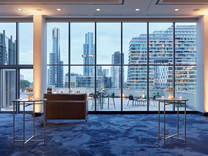 Level 17 of RACV City Club set up for a cocktail event in the evening, with a cocktail station set up inside, and chairs and small tables on the balcony outside.