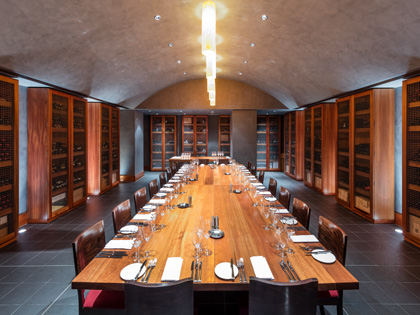 Long dining table surrounded with shelved wine bottles ready for dinner service.