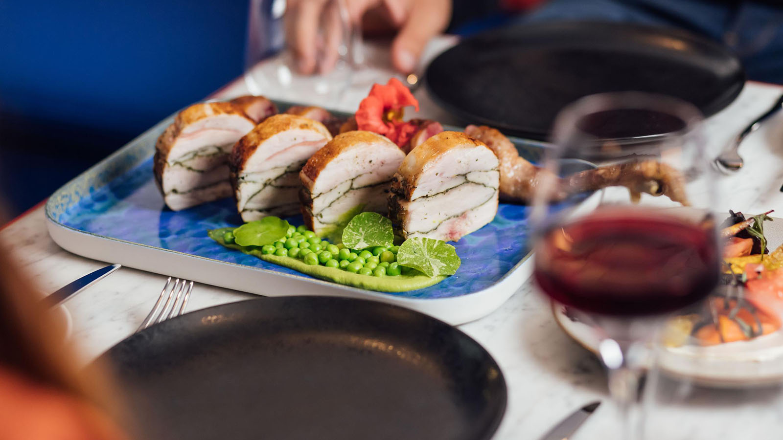 A meal arranged in the middle of a table at Sojourn, one person reaching out to serve.